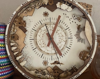 May include: A wooden clock with a circular design featuring the months of the year in French. The clock face has a detailed zodiac design and a sun and moon motif. The clock hands are made of wood and point to the current time.