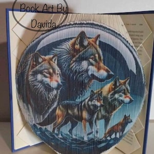 May include: A book art sculpture of a pack of wolves, created by folding the pages of a book. The sculpture is in a circular shape and features a blue background with a white moon. The text "Book Art By Davida" is visible in the top left corner of the image.