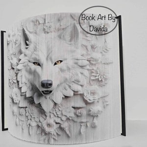 May include: A white wolf's face is partially obscured by white paper flowers. The wolf's eyes are yellow. The image is a book art piece by Davida.