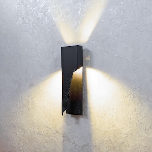 Puede incluir: Un aplique de pared negro con un diseño único y dentado. El aplique proyecta una luz blanca cálida en la pared.