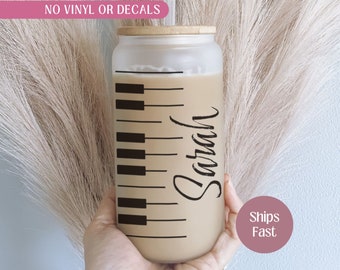 May include: A frosted glass tumbler with a bamboo lid and a black and white piano key design. The tumbler has the name "Sarah" written on it in black cursive.