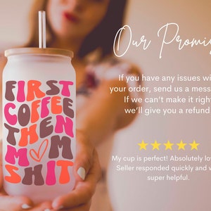 Op de afbeelding: Een witte keramische beker met een roze, oranje en bruine afbeelding met de tekst "First Coffee Then Mom Shit". De beker heeft een bamboe deksel en een doorzichtige rietje.