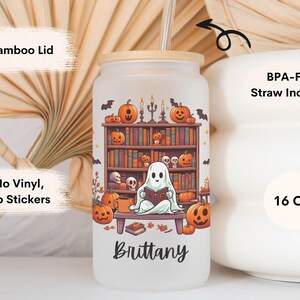 May include: A white 16 ounce reusable tumbler with a bamboo lid and a straw. The tumbler features a ghost reading a book in front of a bookshelf with pumpkins and candles. The text "Brittany" is printed on the bottom of the tumbler.