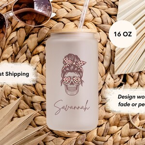 Op de afbeelding: Een 473 ml frosted glazen tumbler met een bamboe deksel en een rietje. De tumbler heeft een ontwerp van een schedel met een knot, die een zonnebril met luipaardprint en een hoofdband draagt. De naam "Savannah" staat onder de schedel. Het ontwerp is op de tumbler gedrukt en zal niet vervagen of afbladderen.
