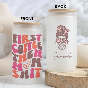 Op de afbeelding: Een witte, gematteerde glazen tumbler met een bamboe deksel en rietje. De voorkant van de tumbler heeft de tekst "First Coffee Then Mom Shit" in roze, oranje en bruin. De achterkant van de tumbler heeft een roze schedel met een luipaardprint bandana en zonnebril. De tekst "Savannah" staat onder de schedel.