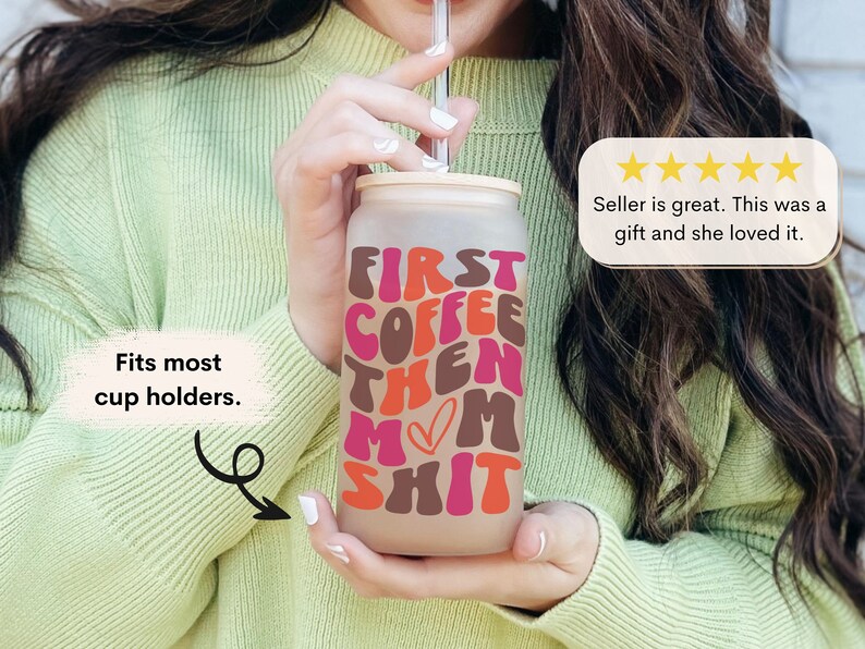 Op de afbeelding: Een frosted glazen beker met een roze, bruine en oranje afbeelding met de tekst "First Coffee Then Mom Shit". De beker heeft een deksel en een rietje. Het past in de meeste bekerhouders.