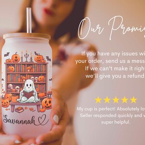 May include: A white tumbler with a Halloween-themed design featuring a ghost reading a book in front of a bookshelf with pumpkins and bats. The tumbler has a bamboo lid and a straw. The name "Savannah" is written on the tumbler.