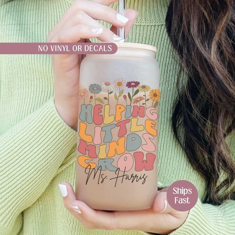 May include: A frosted glass tumbler with a bamboo lid and a straw. The tumbler has a colorful graphic that says "Helping Little Minds Grow" with a floral design and the text "Ms. Harris".