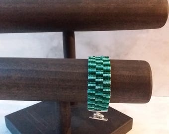 May include: A green beaded bracelet with a silver clasp displayed on a wooden stand.