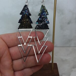 May include: A pair of silver geometric earrings with black and iridescent beaded triangles hanging from them.