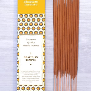 Może przedstawiać: Żółte pudełko kadzideł Bhagwan z napisem "Supreme Quality Masala Incense" i "Dravidian Temple". Pudełko ma kwiatowy wzór. Obok znajduje się kilka brązowych patyczków kadzidła.