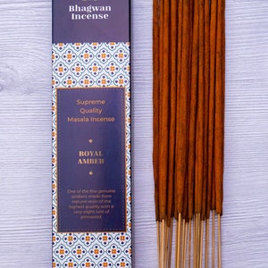 Peut inclure: Une boîte de bâtonnets d'encens Royal Amber de Bhagwan Incense. La boîte présente un motif bleu et blanc avec le texte "Supreme Quality Masala Incense" et "Royal Amber". Le texte "One of the few genuine ambers made from natural resin of the highest quality with a very slight hint of pinewood." est également sur la boîte. Les bâtonnets d'encens sont bruns et ont un parfum de bois naturel.
