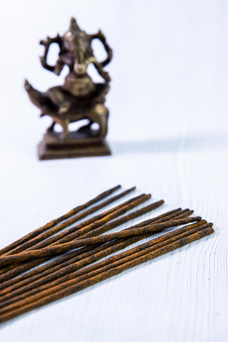 Peut inclure: Un paquet de b&acirc;tonnets d'encens bruns sur une surface en bois blanc. Une petite statue de divinit&eacute; en laiton floue se trouve en arri&egrave;re-plan.