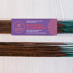 Könnte beinhalten: Zwei Bündel Räucherstäbchen mit braunen Holzbasen und blaugrünen Spitzen. Ein Bündel ist in ein violettes Etikett mit der Aufschrift Monsoon Incense, Botanica Alchemica sowie Text über eine Mischung aus seltenen Kräutern, Harzen und Ölen gewickelt.