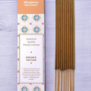 May include: A box of Bhagwan Incense with the words "Supreme Quality Masala Incense" and "Golden Nectar" printed on it. Next to the box are several brown incense sticks.