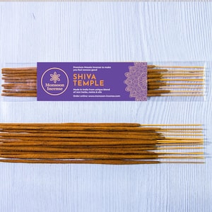 Puede incluir: Palitos de incienso marrones con puntas amarillas, expuestos sobre una superficie de madera blanca. Una etiqueta morada dice "Shiva Temple" con la marca "Monsoon Incense". El incienso está empaquetado en una funda de plástico transparente.