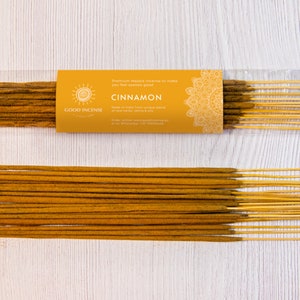 May include: A package of cinnamon incense sticks with a yellow label that reads "Cinnamon" and "Good Incense". The incense sticks are brown with yellow tips, and some are loose next to the package.