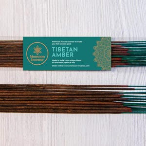 May include: Two bundles of Tibetan Amber incense sticks. The incense sticks are brown with green tips, packaged in a clear plastic sleeve. A teal label reads "Tibetan Amber" with the Monsoon Incense logo.