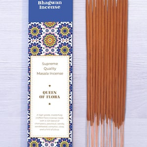 Może przedstawiać: Pudełko kadzidła Bhagwan z napisem "Supreme Quality Masala Incense" i "Queen of Flora". Pudełko ma niebieską górę i kwiatowy wzór. Po prawej stronie znajduje się wiązka brązowych patyczków do kadzidła.