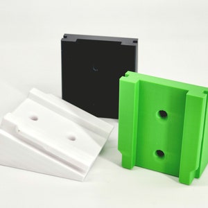 May include: Three plastic wall mounts in different colors: white, black, and green. Each mount has two holes for attaching to a wall.