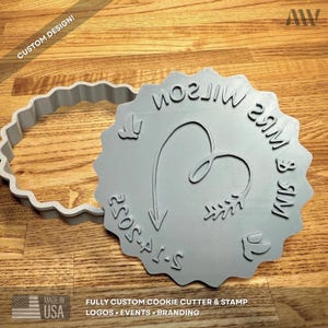 May include: A light gray circular cookie cutter and matching stamp set with a scalloped edge. The stamp features the text MRS WILSON & MR, the date 2-14-2025, a heart-shaped arrow, and two small bird icons embossed on the flat surface.