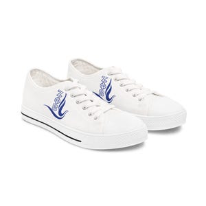 May include: White canvas sneakers with blue and white logo detail. The low-top shoes have white laces, a white rubber toe cap, and a black stripe along the sole. The shoes are a casual style.