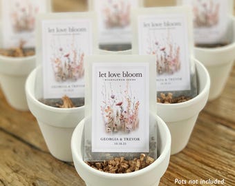 May include: White ceramic pots filled with seed packets. Each packet has the text "let love bloom" and the names "Georgia & Trevor" with a date. The packets contain wildflower seeds.