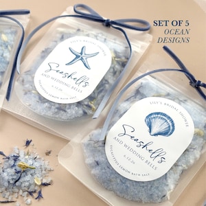 May include: Clear pouches filled with blue bath salts, labeled "Seashells and Wedding Bells" with a starfish and seashell design. Each pouch is tied with a blue ribbon. Text on the label reads "Lily's Bridal Shower" and "Eucalyptus Lemon Bath Salt".
