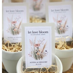 May include: White ceramic pots filled with dried straw, holding packets of wildflower seeds. Each packet features floral illustrations and the text "let love bloom," along with names and a date. The image is labeled "Wildflower WEDDING FAVORS."