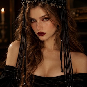 May include: A black headpiece featuring a row of dark floral embellishments and long, dangling beaded strands that frame the face. The accessory is constructed with intricate black beadwork and metallic leaf accents, creating a layered effect.