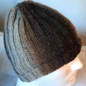 May include: A ribbed knit beanie in a gradient of brown and gray hues. The hat is made of a textured yarn, with vertical ribbing creating a striped effect. The beanie is a casual accessory.