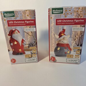 May include: Two boxes of LED Christmas figurines. The boxes are red and white with a festive design. The figurines are a Santa Claus and a snowman. The boxes say "LED Christmas Figurine" and "Cheerful, ambience-enhancing decoration".