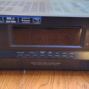 Pode incluir: Receptor AV Sony 5.1 preto com um grande visor e vários botões. Possui um grande botão de volume e um seletor de entrada. Texto: "5.1 AV Receiver", "100W x 5", "Total 500W" e "Digital Audio/Video Control Center".