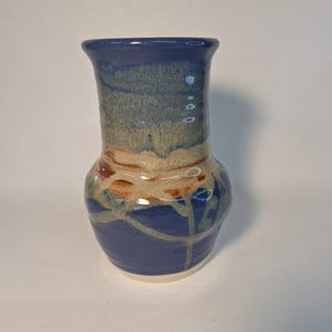 May include: A small, blue ceramic vase with a white rim and brown and green accents. The vase has a rounded body and a narrow neck.