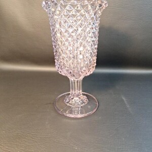May include: A clear, pink glass vase with a diamond pattern and a scalloped rim. The vase has a pedestal base.