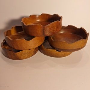 May include: Set of four wooden bowls with a wavy edge. The bowls are stacked on top of each other and are made of a light brown wood.