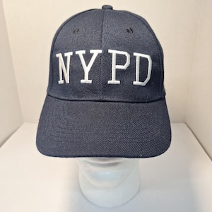 May include: A navy blue baseball cap with white embroidered lettering that reads "NYPD".