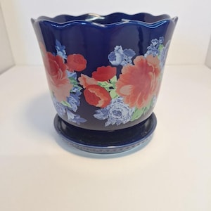 May include: A navy blue ceramic flower pot with a matching saucer. The pot features a scalloped rim and is decorated with red and blue floral patterns. A decorative item for indoor or outdoor use.