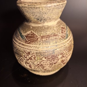 May include: A small, brown ceramic vase with a decorative design. The vase has a wide mouth and a rounded body. The design features geometric shapes and floral motifs.