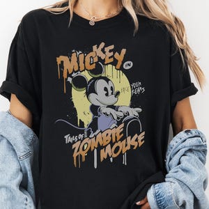 May include: Black t-shirt featuring a distressed graphic of Mickey Mouse with sunglasses, the text "Mickey" and "Tales of Zombie Mouse". The design has a vintage, comic book style. The shirt is a relaxed fit.