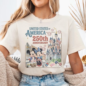 A woman wearing a white t-shirt with a graphic of Mickey Mouse and Minnie Mouse celebrating the United States of America's 250th anniversary.