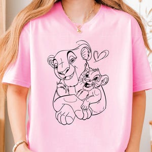 May include: A pink t-shirt with a black line drawing of Simba and Mufasa from The Lion King. The drawing shows Simba being held by Mufasa with a heart above their heads.