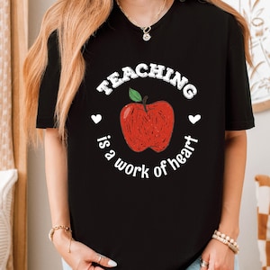 a woman wearing a teaching is a work of heart t - shirt