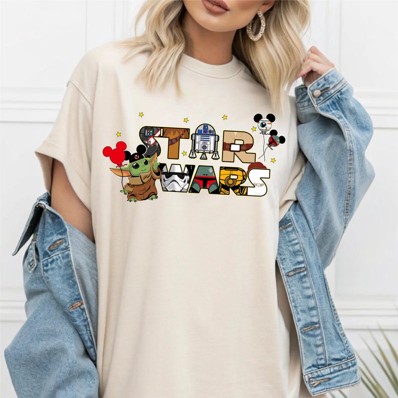 A woman wearing a white t-shirt with a Star Wars logo and various Star Wars characters, including Baby Yoda, a character from the Star Wars franchise.
