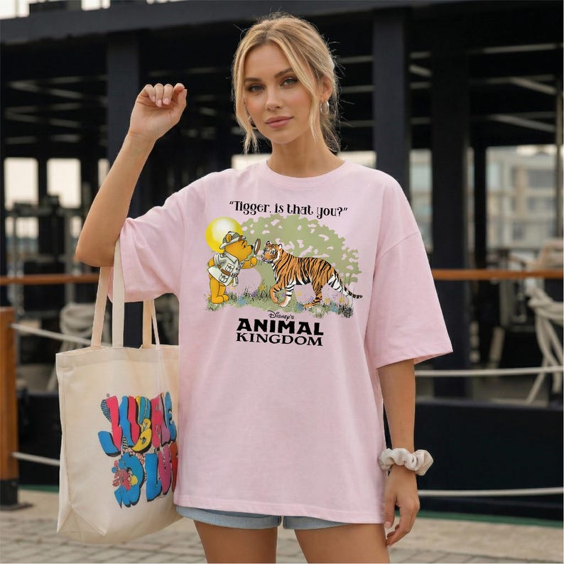 A woman wearing a pink t-shirt with a cartoon tiger and text, standing in front of a building.