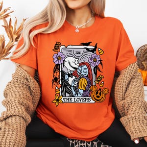 A woman wearing an orange t-shirt with a graphic design featuring characters from the movie "The Jack Skellington".