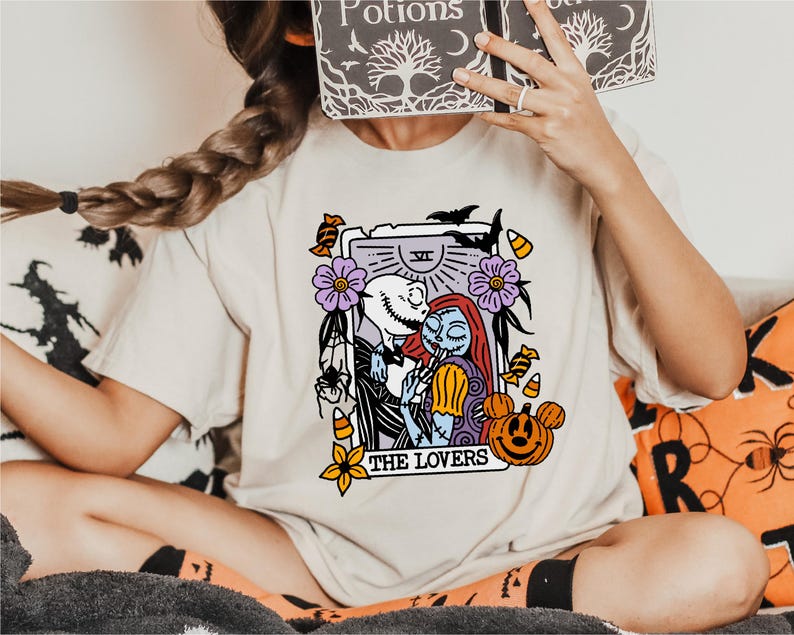 A person is sitting on a couch wearing a white t-shirt with a graphic design featuring characters from the movie "The Jack Skellington".