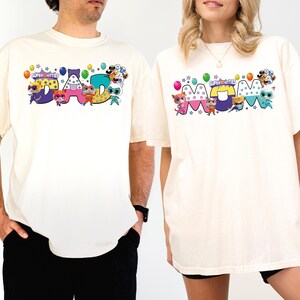 A man and a woman wearing matching white t-shirts with colorful cartoon characters and text.