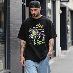 A man wearing a black t-shirt with a graphic of Buzz Lightyear from the Toy Story franchise, standing on a city street.