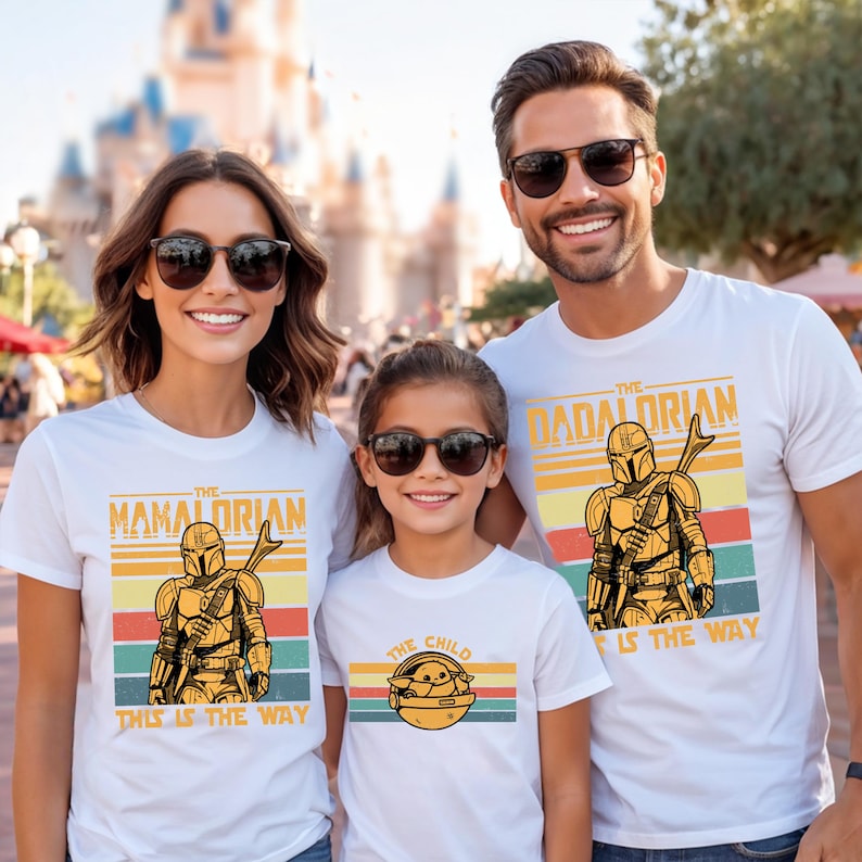 A family of three, consisting of a woman, a man, and a child, is standing together and smiling. They are all wearing white t-shirts with the same design featuring a character from the Star Wars franchise.